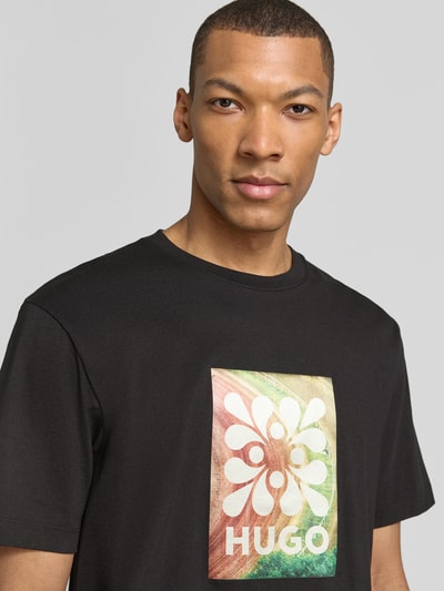 Männermodel trägt Regular Fit T-Shirt aus reine Baumwolle Modell 'DAMORU' von HUGO in Schwarz mit Foto-Print und Label-Schriftzug, Nahaufnahme Oberkörper.