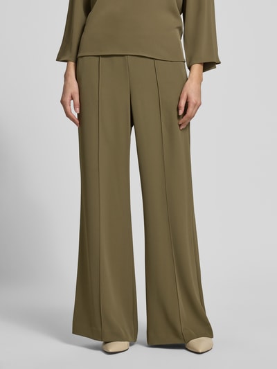 Vrouwenmodel draagt stoffen broek met elastische materiaalmix, flared fit, elastische band, siernaden van comma, nahaufnahme onderlichaam.
