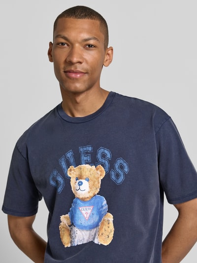 Männermodel trägt T-Shirt mit Motiv-Print und Rundhalsausschnitt von Guess aus reiner Baumwolle in Regular-Fit, Nahaufnahme Oberkörper.