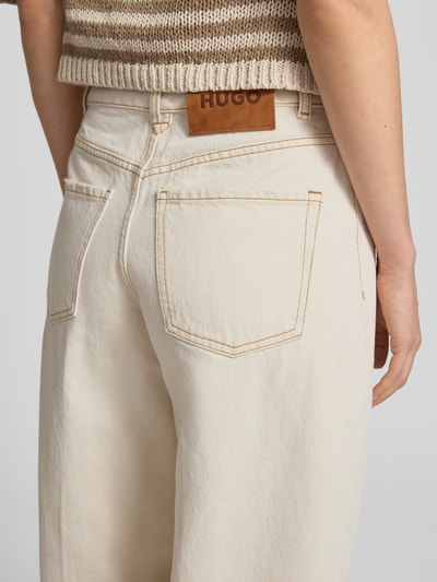 Kobieta nosi Loose Fit Jeans aus reiner Baumwolle Modell Gimine_5 von HUGO w kolorze jasnego denimu, 5 kieszeni, wysoki stan, detal skórzany, materiał twill, widok z tyłu, detal tylnej części.
