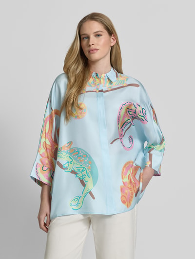 Frauenmodel trägt Bluse mit Hemdblusenkragen und 3/4-Arm von HERZENS, lockerer Schnitt, hellblaue Farben mit buntem Muster, Ganzkörperansicht von vorne.