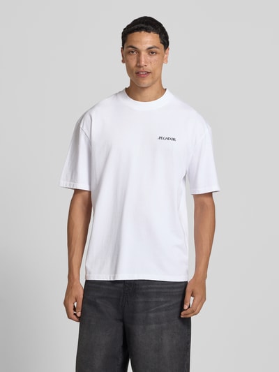 Männermodel trägt wit oversized T-shirt van Pegador, puur katoen, model 'Miles' met labelprint, ronde hals, heren, ruglengte maat M 70 cm, Ganzkörperansicht van voren.