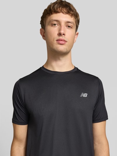 Männermodel trägt T-Shirt mit Label-Print Modell 'ESSENTIAL' von New Balance in Schwarz, glatte Struktur, Nahaufnahme Oberkörper, gerader Schnitt, Rundhalsausschnitt, Rückenlänge bei Größe M 71 cm.
