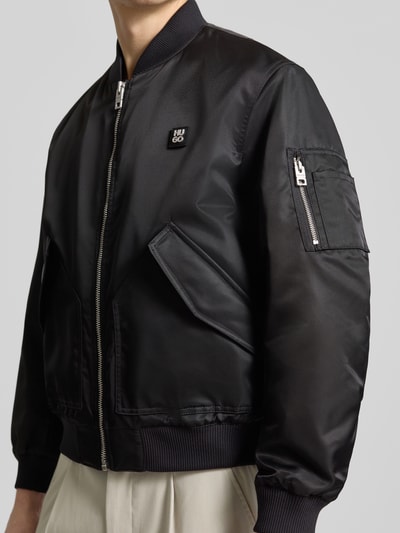Männermodel trägt Regular Fit Bomberjacke mit Label-Applikation Modell 'Badam2611' von HUGO, schwarze Twill-Optik, Nahaufnahme Oberkörper.