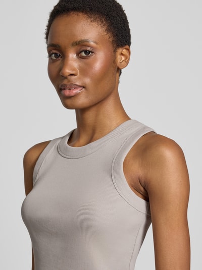 Kobiece modelka nosi Skinny Fit Tanktop aus reiner Baumwolle od DRYKORN w kolorze jasnoszarym, efekt prążkowania, okrągły dekolt, kontekst: top z bawełny, krój skinny fit, Długość tyłu w rozmiarze S: 54 cm, zbliżenie na górną część ciała.