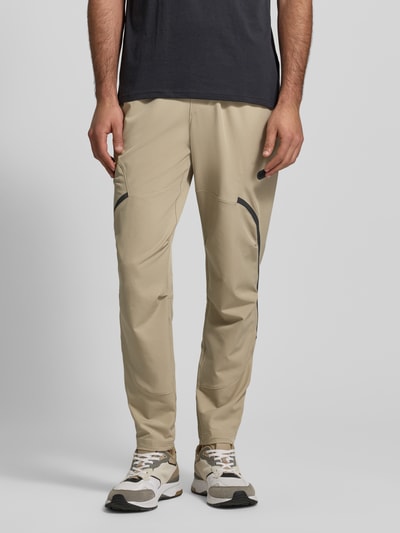 Männermodel trägt Regular Fit Sweatpants mit Logo-Print Modell 'Unstoppable' von Under Armour aus elastischem Material-Mix in Beige, Cargo-Taschen mit Reißverschluss, elastischer Bund, Ganzkörperansicht von vorne.