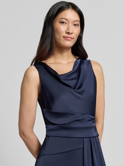 Frauenmodel trägt Abendkleid mit Wasserfallausschnitt von Rinascimento in Dunkelblau, Material-Mix mit Stretch-Anteil, taillierte Passform, Raffungen, Stoffgürtel, Rückseitiger Reißverschluss, Nahaufnahme Oberkörper.