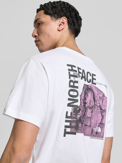 Männermodel trägt T-Shirt mit Logo und Rundhalsausschnitt von The North Face, weiß mit lila Print, Baumwoll-Mix, Regular Fit, Ganzkörperansicht Rückansicht.