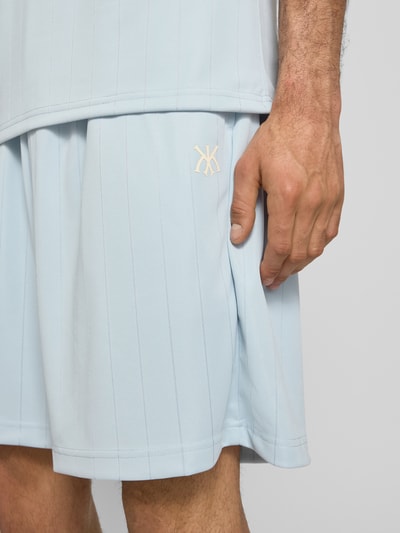Mężczyzna nosi szorty Relaxed Fit Shorts mit elastischem Bund Modell 'Insignia' od KARL KANI, detal z logo, jasnoniebieski kolor, długość wewnętrzna nogawki 20 cm, szerokość w rozmiarze M 37 cm, detailaufnahme uda