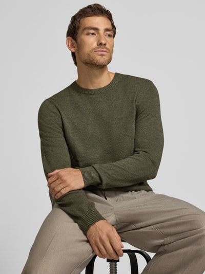 Männermodel trägt Kaschmirpullover mit gerippten Abschlüssen von Christian Berg Men in Olivgrün, feine Stricktextur, Nahaufnahme Oberkörper. Reines Kaschmir, gerader Schnitt, Rundhalsausschnitt, Rücklänge und Ärmellänge je 72 cm bei Größe M.