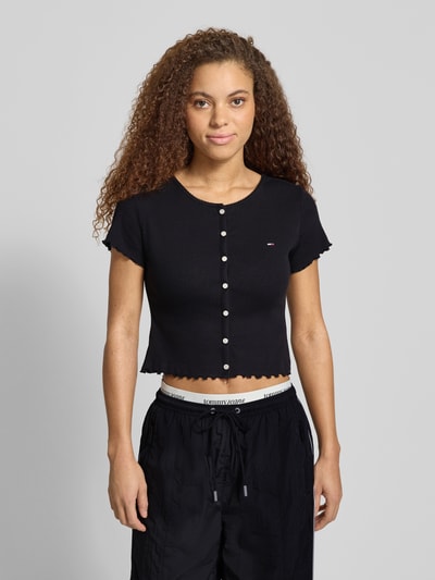 Modelka kobieca nosi Slim Fit T-Shirt aus Baumwoll-Mix od Tommy Jeans, czarny, krój slim fit, krótki rękaw, logo, ripp, u-boot, frill, widok na górną część ciała z przodu.