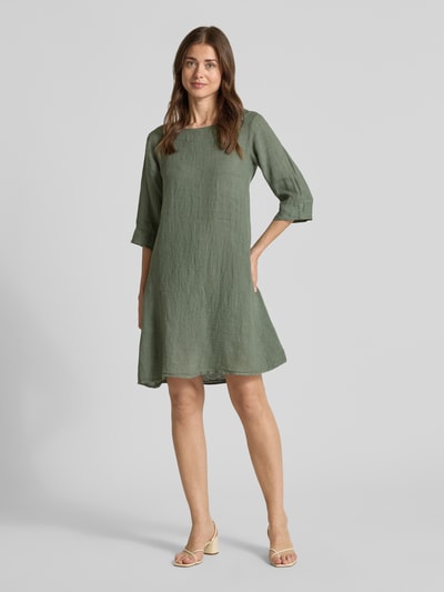 Frauenmodel trägt Leinenkleid mit Rundhalsausschnitt Modell 'Le44tizia' von ZABAIONE in A-Linie, Minikleid, 3/4-Arm, Ganzkörperansicht von vorne, Rückenlänge 82 cm, Brustweite 43 cm, Ärmellänge 28 cm, grüner Farbton, strukturierte Leinen-Oberfläche.