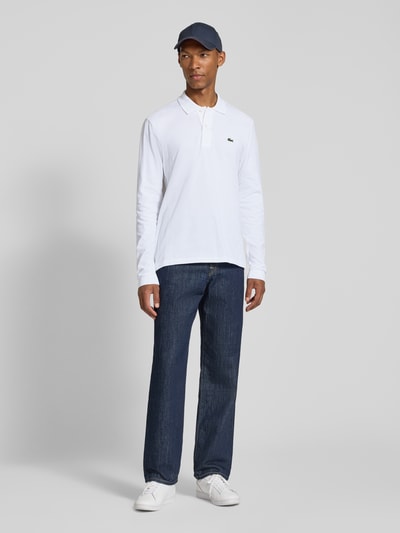 Männermodel trägt Regular Fit Poloshirt aus reiner Baumwolle von Lacoste in Weiß, kombiniert mit Jeans, Ganzkörperansicht von vorne, Herren Poloshirt von Lacoste