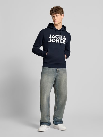 Männermodel trägt Hoodie mit Label-Print und Känguru-Tasche von Jack & Jones, dunkelblau, Baumwoll-Mix, Regular Fit, Ganzkörperansicht von vorne.