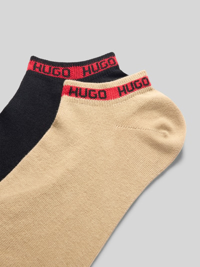 Produktfoto, Socken aus Baumwoll-Mix von HUGO für Herren in Beige und Schwarz mit rotem Markenlogo, weiche Textur auf grauem Hintergrund