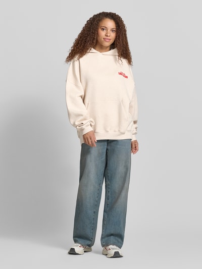 Frauenmodel trägt Hoodie mit Statement-Print Modell 'Love Club' von Karo Kauer in Reine Baumwolle, Oversized-Fit, Kapuze, Känguru-Tasche, Ganzkörperansicht von vorne.