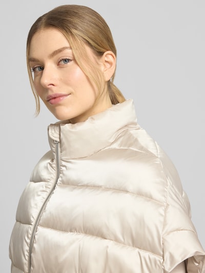 Vrouwenmodel draagt Steppweste mit Stehkragen van Milano Italy, relaxed fit, lichte beige tint, glanzende textuur, close-up bovenlichaam.