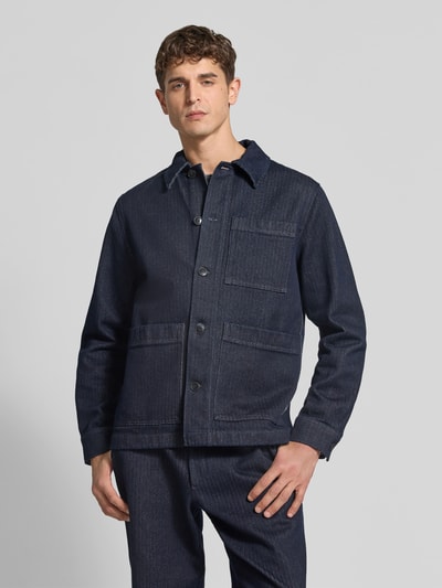 Męski model nosi Regular Fit Jacke aus reiner Baumwolle od Closed, ciemnoniebieski denim, z naszytymi kieszeniami i zapięciem na guziki, krój regular fit, widok całej sylwetki z przodu. Szerokość w rozmiarze M: 48 cm, długość tyłu: 64 cm, długość rękawa: 66 cm.