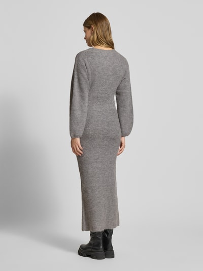 Kobiece model prezentuje sukienkę z dzianiny z dekoltem w serek i listwą guzikową od Gina Tricot, mieszanka materiałów z domieszką wełny z alpaki, prosty krój, długa sukienka, długość tyłu 138 cm, szerokość klatki piersiowej 40 cm, długość rękawów 66 cm, widok całej sylwetki z tyłu.