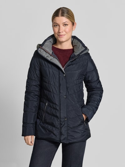 Vrouwenmodel draagt Jacke in Stepp-Optik met Capuchon van FUCHS SCHMITT, getailleerde pasvorm, steekzakken met ritssluiting, gevoerde opstaande kraag, ruglengte bij maat 36: 74 cm, schouderbreedte: 40 cm, borstwijdte: 48 cm, mouwlengte: 64 cm, donkerblauw met lichte textuur, stiksels, volledig zichtbare voorkant, close-up van bovenlichaam.
