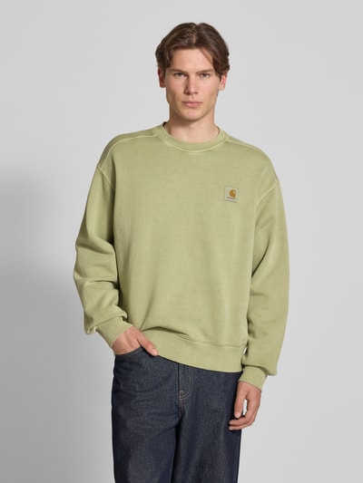 Männermodel trägt Sweatshirt mit Label-Detail Modell 'Nelson' von Carhartt Work In Progress in Grün, Reine Baumwolle, Relaxed-Fit, Rundhalsausschnitt, Ganzkörperansicht von vorne, Rückenlänge 68 cm, Ärmellänge 63 cm.