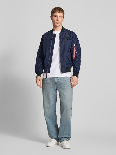 Męski model nosi Regular Fit Bomberjacke mit Logo-Patch od Alpha Industries, granatowy kolor, kieszenie, zamek; całkowity widok z przodu