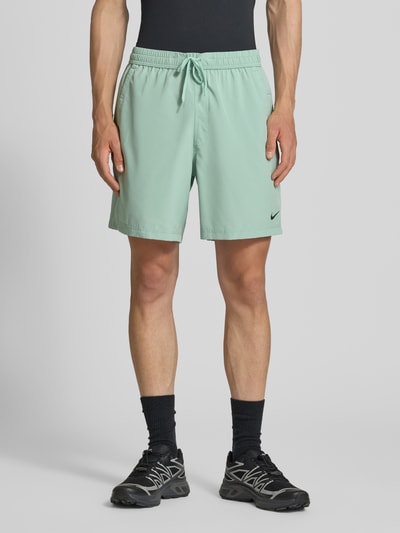 Mannenmodel draagt Shorts met Logo-Print en steekzakken van NIKE TRAINING in mintgroen, recht model, elastische band met tunnelkoord, logoprint, bandwijdte maat M 41 cm, binnenbeenlengte 19 cm. Ganzlichaansicht van voren.