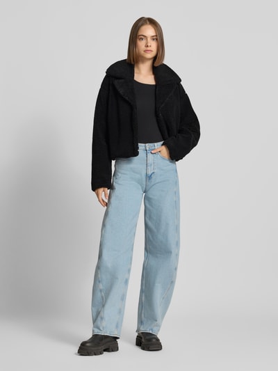 Frauenmodel trägt Cropped Jacke aus Teddyfell Modell 'Nati' von NOISY MAY®, schwarz, weiche Struktur, kombiniert mit Jeans, Ganzkörperansicht von vorne.