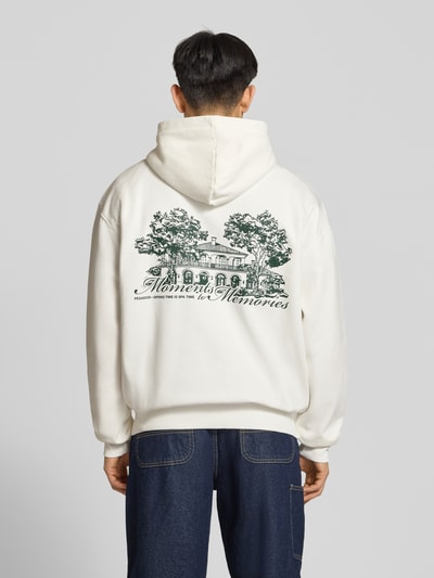 Männermodel trägt Oversized Sweatjacke mit Label-Print Modell 'Rochefort' von Pegador aus Baumwoll-Mix, cremefarben mit Kapuze, Ganzkörperansicht Rückansicht.