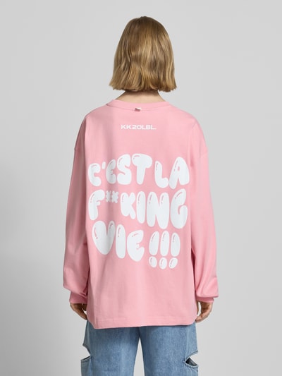 Frauenmodel trägt Sweatshirt mit Logo-Print von Karo Kauer in Rosa mit weißem Print, lockerer Schnitt, reine Baumwolle, Ganzkörperansicht Rückansicht.