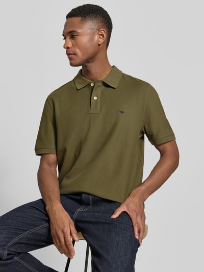 Męski model nosi Regular Fit Poloshirt mit Logo-Stitching od Fynch-Hatton z czystej bawełny, oliwkowy kolor, kołnierzyk polo, krótki rękaw, długość tyłu w rozmiarze M: 70 cm, widok całej sylwetki z przodu.