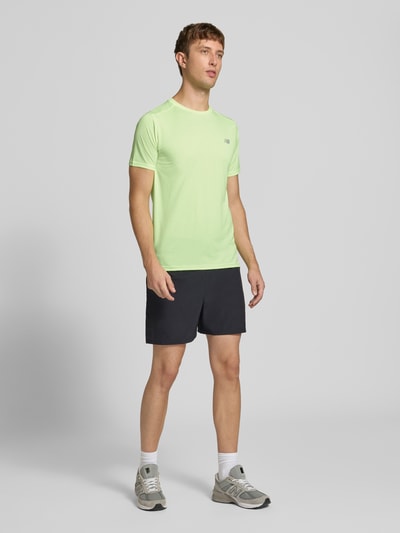 Männermodel trägt Funktionsshirt mit Rundhalsausschnitt und Logo von New Balance, hellgrün, schwarze Shorts, Regular Fit, Ganzkörperansicht von vorne, Rückenlänge bei Größe M 69 cm.