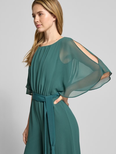 Frauenmodel trägt Jumpsuit aus fließendem Stoff mit Bindegürtel von Vera Mont in Grün, Chiffon, Nahaufnahme Oberkörper. Rückenlänge 146 cm, Brustweite 33 cm, Ärmellänge 30 cm, Gesamtlänge 147 cm, Innenbeinlänge 81 cm.