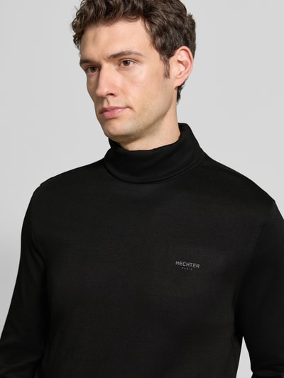 Männermodel trägt schwarzes Longsleeve mit Rollkragen von HECHTER PARIS aus reiner Baumwolle, Label-Details, Nahaufnahme Oberkörper.