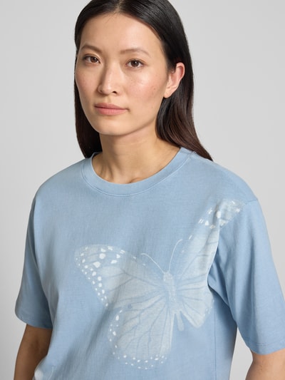 Frauenmodel trägt Relaxed Fit T-Shirt mit Motiv-Print von Jake*s Casual, reine Baumwolle, Statement-Print, Rundhalsausschnitt, Rückenlänge 53 cm bei Größe S, hellblau mit Schmetterling-Motiv, Nahaufnahme Oberkörper.