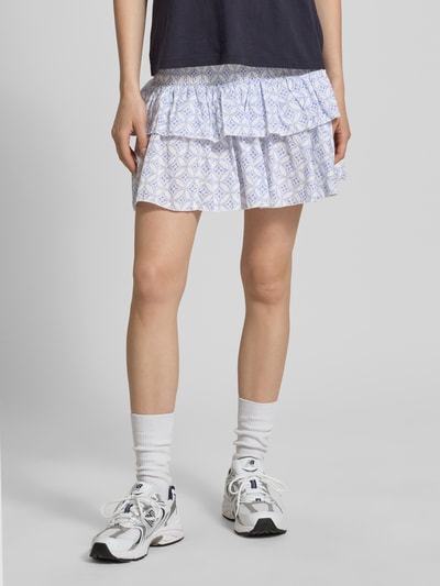 Frauenmodel trägt Ausgestellter Mini-Rock mit Volants Modell 'ZOEY' von Only, Optik: Allover-Muster, Regular-Fit, Mini-Länge, florales Muster, gesmokter Bundabschluss, Material: reine Baumwolle; Weiß- und Blautöne, glatte Textur, Ganzkörperansicht von vorne.