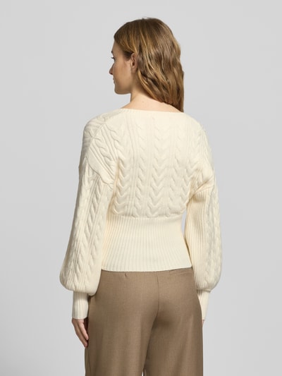 Modelka nosi Strickjacke mit Knopfleiste od Gina Tricot, kremowy kolor, wzór warkoczowy, krój regular fit, widok całej sylwetki z tyłu.