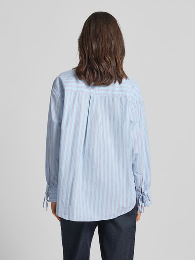 Frauenmodel trägt Oversized Hemdbluse aus reiner Baumwolle von Tom Tailor Denim, wzór w paski, popelina, jasnoniebieski, naszywka z logo, krój oversized, kołnierzyk koszulowy, dekolt w serek, listwa guzikowa, długi rękaw z mankietem i wiązaniem, zaokrąglone wykończenie, materiał: czysta bawełna, Ganzkörperansicht Rückansicht.