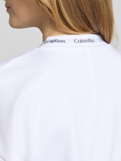 Frauenmodel trägt Comfort Fit T-Shirt mit Label-Schriftzug von Calvin Klein Jeans in Weiß, glatte Struktur, Nahaufnahme Rückenansicht. Damen T-Shirt.