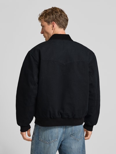 Männermodel trägt Jacke mit Reißverschluss und Label-Detail Modell 'Santa Fe' von Carhartt Work In Progress aus reiner Baumwolle in Schwarz, ganzkörperansicht Rückansicht
