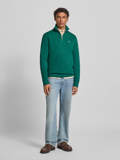 Männermodel trägt Sweatshirt mit Stehkragen und Reißverschluss von Gant in Grün, aus Baumwoll-Mix, Regular-Fit, Ganzkörperansicht von vorne.