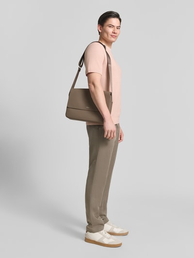 Männermodel trägt Umhängetasche mit Label-Applikation von Lacoste, Optik: Unifarben, rechteckig, genarbtes Leder, Ganzkörperansicht von vorne.