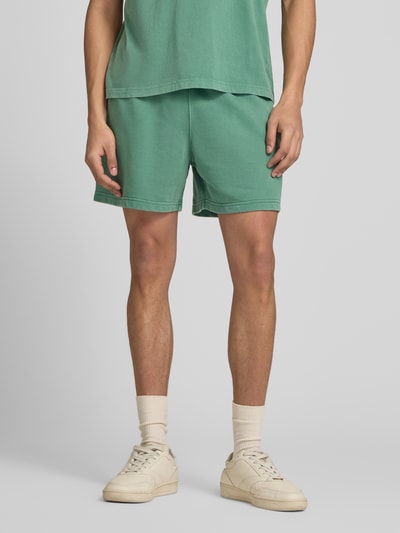 Männermodel trägt grüne Sweatshorts mit Eingrifftaschen von CHAMPION, Baumwoll-Mix, regular fit, Nahaufnahme Oberkörper bis Knie.