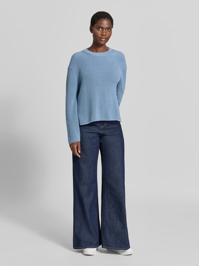 Modelka kobieca nosi niebieski sweter Loose Fit Pullover aus reiner Baumwolle od Marc O'Polo, szerokie dżinsy, białe buty, widok całej sylwetki z przodu.