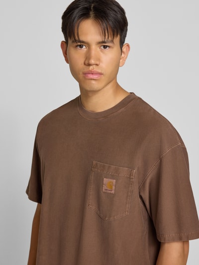 Männermodel trägt Regular Fit T-Shirt aus reiner Baumwolle Modell 'Loose Pocket' von Carhartt Work In Progress in Braun mit Brusttasche, Nahaufnahme Oberkörper.