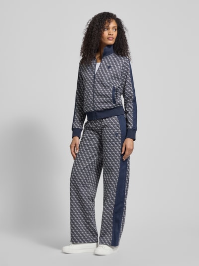 Kobiece modelka nosi Sweatjacke mit Stehkragen Modell 'MAYA' od Guess Activewear, krój regular fit, granatowe i szare wzory, ściągacze, zamek, detale z logo, kieszenie boczne, widok całej sylwetki z przodu