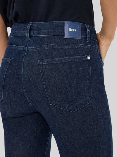 Frauenmodel trägt Bootcut Jeans mit Fransen Modell 'SHAKIRA' von Brax, dunkelblauer Baumwoll-Mix mit Stretch-Anteil, Gesäßtasche, Fransen-Saum, verkürzte Passform, Nahaufnahme Rückansicht.
