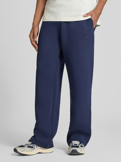 Männermodel trägt Straight Fit Sweatpants Baumwoll-Mix von REVIEW in Dunkelblau mit Label-Print, elastischem Bund und Gesäßtasche, Nahaufnahme Unterkörper.
