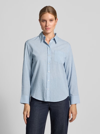 Frauenmodel trägt Relaxed Fit Hemdbluse aus reiner Baumwolle Modell 'CHUACKUA' von MANGO mit Karomuster, hellblau und weiß, durchgehende Knopfleiste, Brusttasche, Hemdblusenkragen, langärmelig, strukturierte Textur, Ganzkörperansicht von vorne.