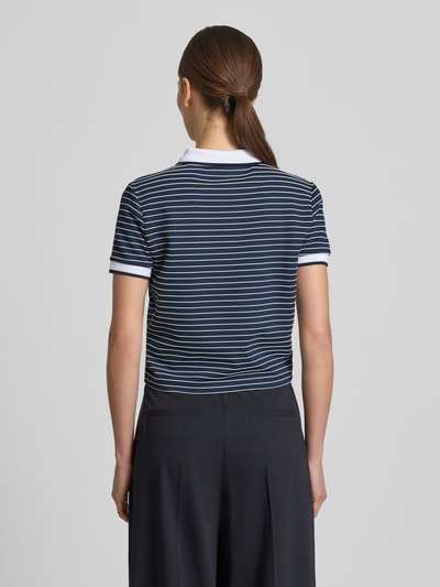 Modelka nosi koszulkę polo Cropped Poloshirt aus Viskose-Mix Modell 'ALPHONSINE' od Guess, mieszanka wiskozy z dodatkiem streczu, krój krótki, wzór w paski, listwa guzikowa, długość tyłu w rozmiarze S: 49 cm, widok całej sylwetki z tyłu.